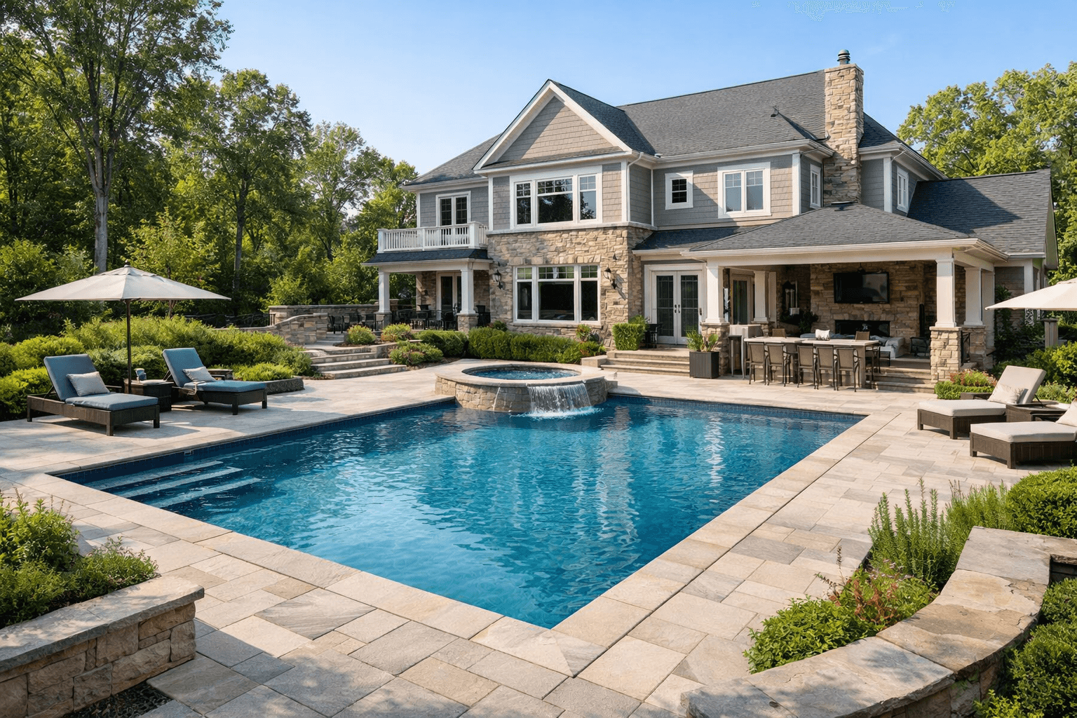 Luxury inground pool with spa waterfall feature and travertine deck beside a large stone and shingle home in Virginia or Maryland