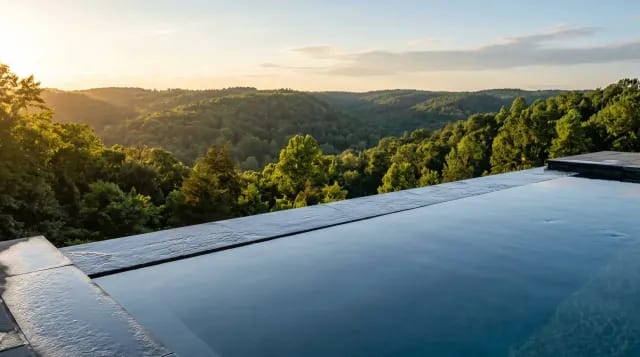 Infinity-edge pool with water sheeting over a vanishing edge toward a wooded valley