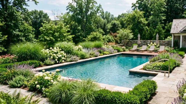Inground pool framed by lush integrated planting beds and ornamental grasses