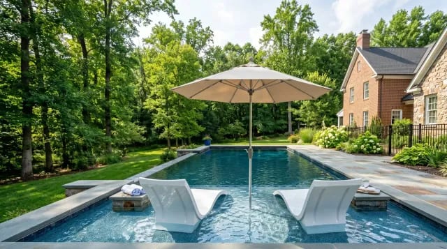 Pool tanning ledge with white in-water lounge chairs and an umbrella in a Virginia backyard