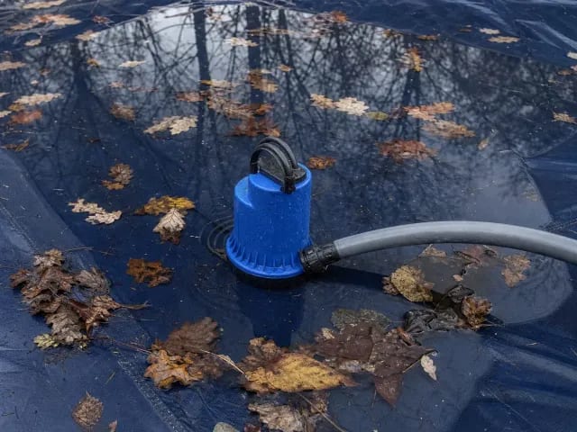 Submersible cover pump sitting in standing water and wet leaves on a solid pool cover