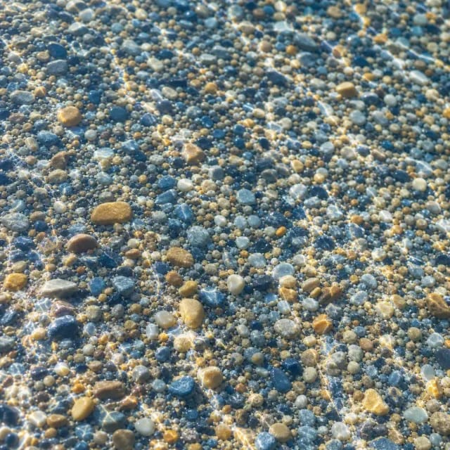 Closeup of blue and tan pebble aggregate pool finish under clear rippling water