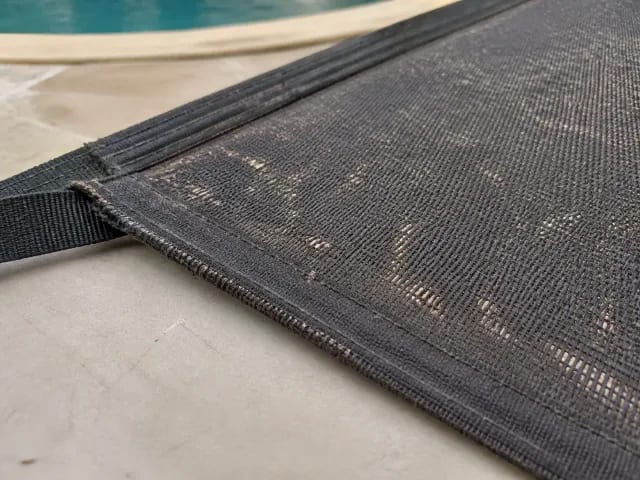 Faded safety-cover mesh showing scattered pinholes and a weakened stitched edge