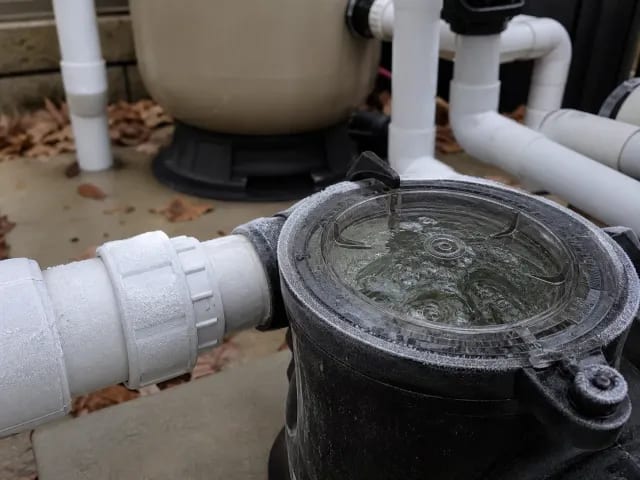 Frost on a running pool pump strainer lid and PVC union, with a sand filter behind