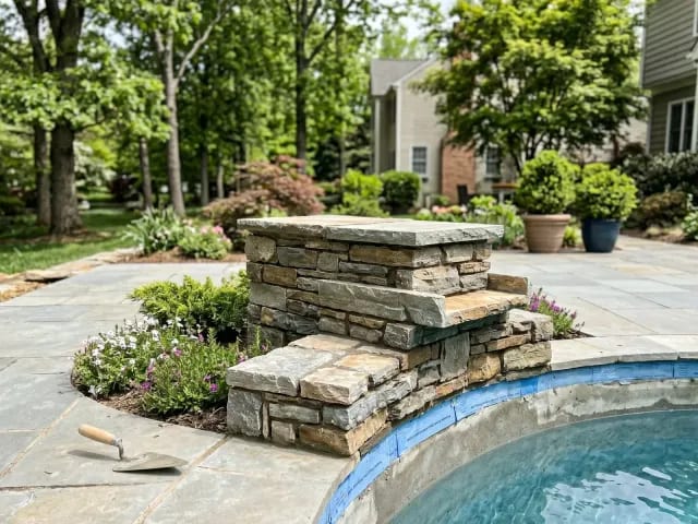 New stacked stone pool water feature being installed beside an inground pool