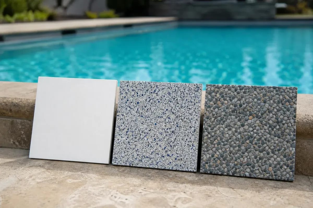 Plaster, quartz, and pebble pool finish sample boards side by side on stone coping at the pool edge