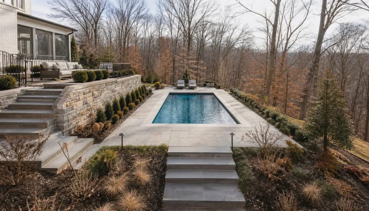Terraced inground pool with stone retaining walls on a wooded sloped lot