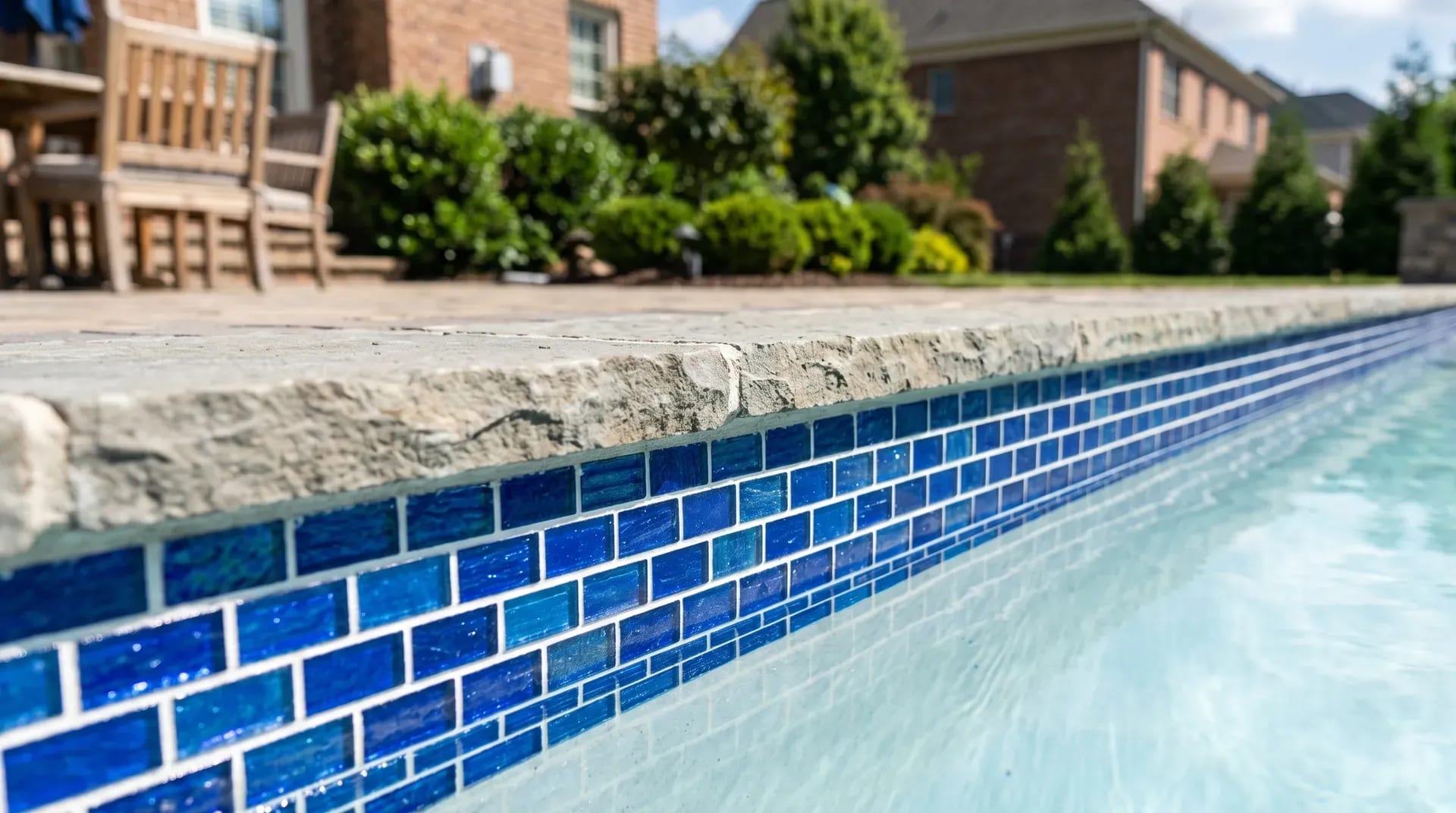 Brand-new blue glass-mosaic waterline tile band along an inground pool edge